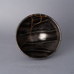 Top view into a black Arita ware footed bowl, the 24K gold kintsugi seam branching across the interior against hand-painted striations in varying shades of black and pewter.