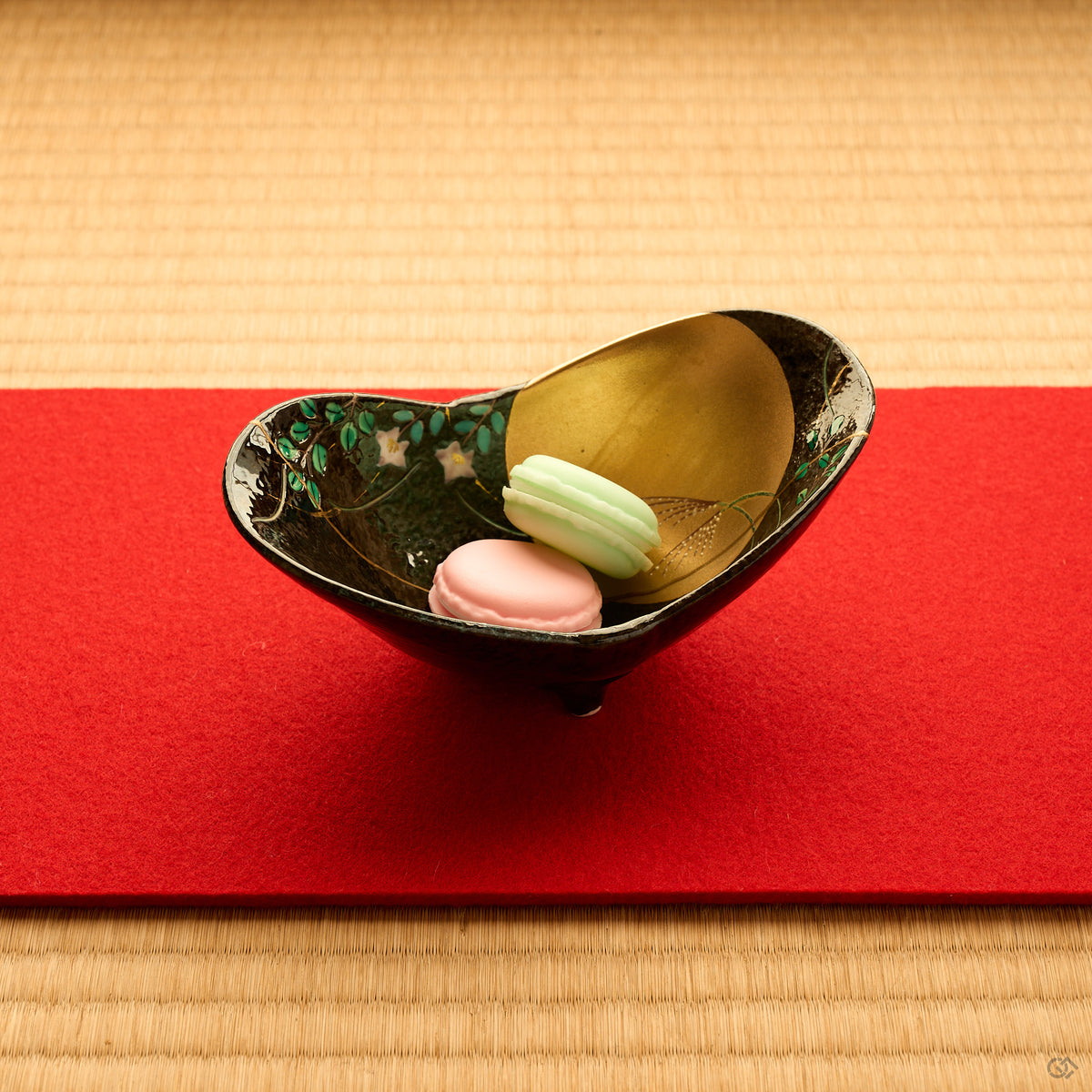 Kintsugi Arita ware bowl holding two macarons on a red cloth over tatami, rejoined with natural urushi, the 24K gold seam beside the painted moon, in-use view.