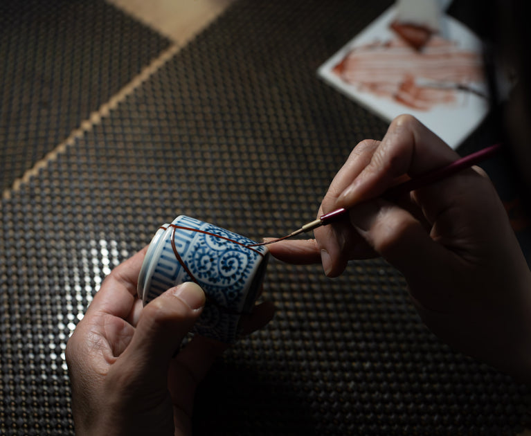 Kintsugi artist applying urushi lacquer with a fine brush to a blue-and-white Japanese porcelain cup