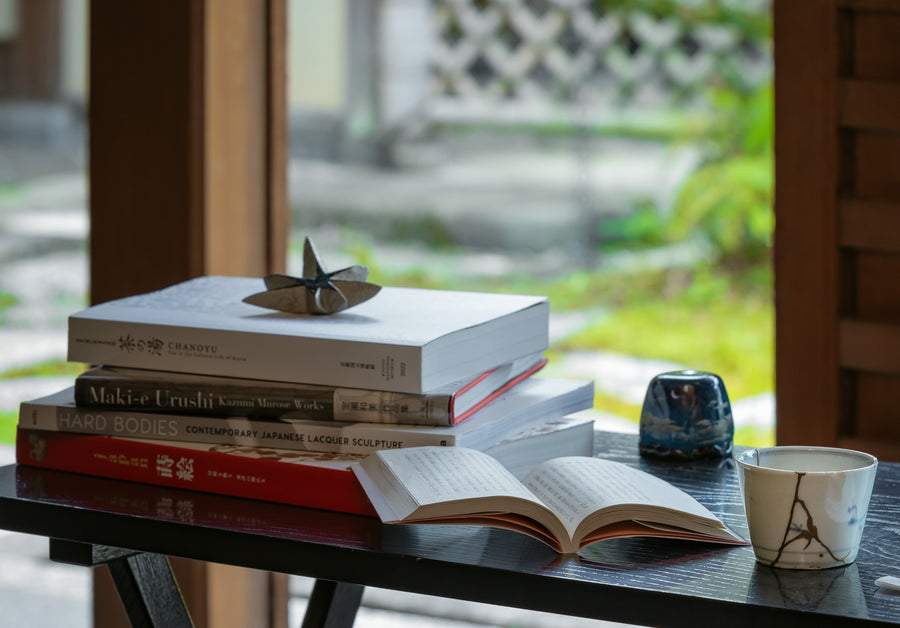 Close-up of The Book of Tea with Kintsugi pieces on a black table, framed by garden light.