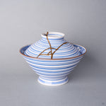 Kintsugi bowl with lid in Arita sometsuke porcelain, natural urushi and 24K gold lines descending from the knob across the blue rings of the lid, front view.