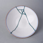 Kintsugi bowl lid interior in Arita porcelain, the fracture finished in green colored natural urushi with tiny blue triangles, opposite its 24K gold face.
