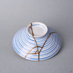 Kintsugi bowl lid in Arita porcelain seen alone, natural urushi and 24K gold lines branching from the ring knob across the blue rings toward the edge.