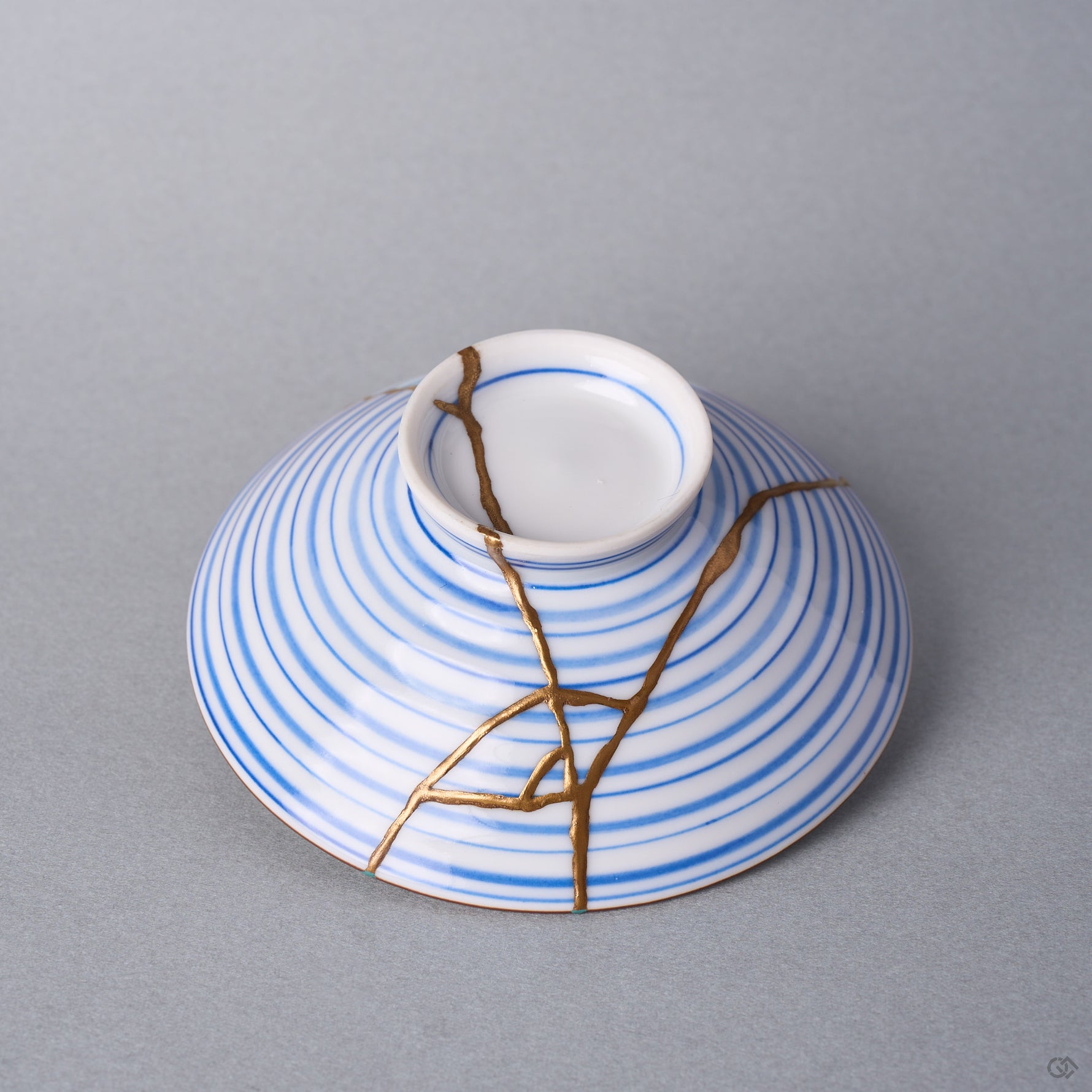 Kintsugi bowl lid in Arita porcelain seen alone, natural urushi and 24K gold lines branching from the ring knob across the blue rings toward the edge.