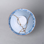 Kintsugi bowl with lid in Arita porcelain from above, natural urushi and 24K gold lines crossing the concentric blue rings of the lid inside the wave band.