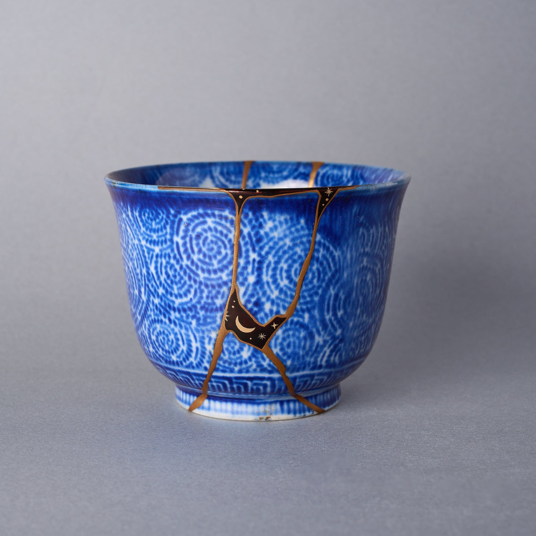 Ko-Imari cup with authentic kintsugi repair seams finished in 24K gold, cobalt spirals, and moon-and-star urushi decoration.