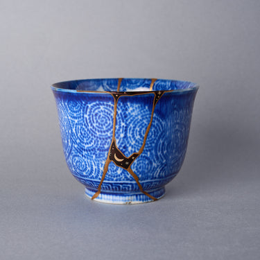 Ko-Imari cup with authentic kintsugi repair seams finished in 24K gold, cobalt spirals, and moon-and-star urushi decoration.
