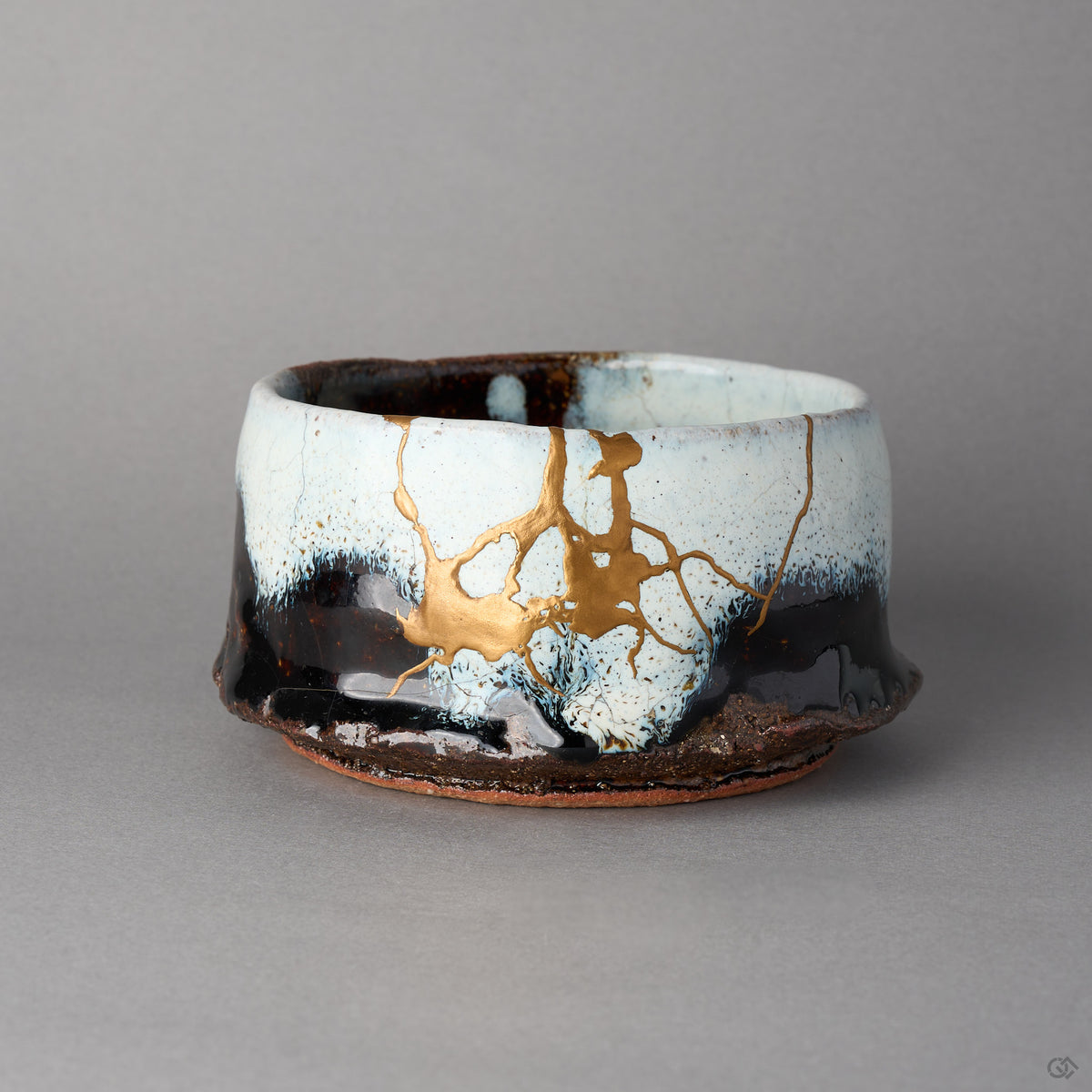 Kintsugi matcha bowl in Karatsu stoneware, white glaze over black, rejoined with natural urushi, a 24K gold field and branching seams, front view.