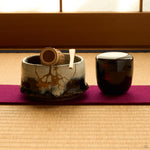 Kintsugi matcha bowl in Karatsu stoneware on tatami with a bamboo whisk, scoop and lacquer caddy, rejoined with natural urushi, 24K gold seams in front.