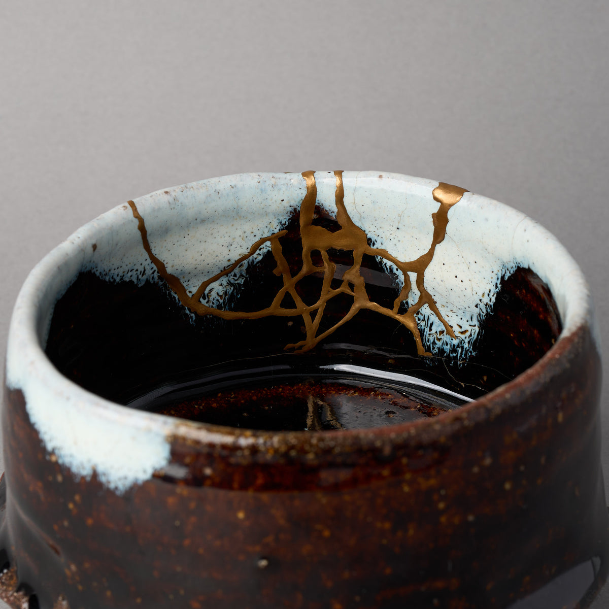 Kintsugi matcha bowl in Karatsu stoneware, rejoined with natural urushi, 24K gold lines descending from the rim and knotting above the well, interior close-up.