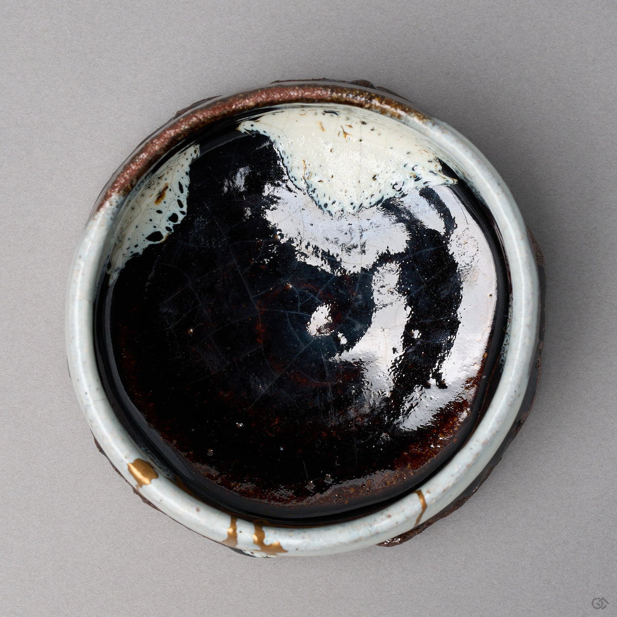 Kintsugi matcha bowl in Karatsu stoneware, the glossy black well and a pool of white glaze, rejoined with natural urushi, two 24K gold rim marks, top view.