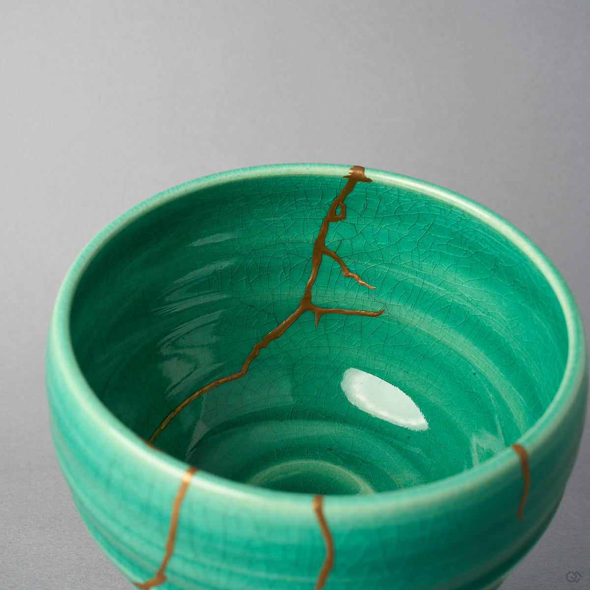 Kintsugi matcha bowl interior where urushi and 24K gold lines fork above the emerald crackle basin, close-up view.