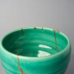 Kintsugi matcha bowl rim in close-up: small gold points mark restored chips while urushi and 24K gold lines descend inside.