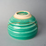 Kintsugi matcha bowl from below: a long urushi and 24K gold line circles the ridged emerald body above the unglazed foot.