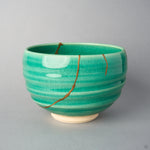 Kintsugi matcha bowl side view: two urushi and 24K gold lines descend the spiral-ridged emerald crackle glaze from the rim.