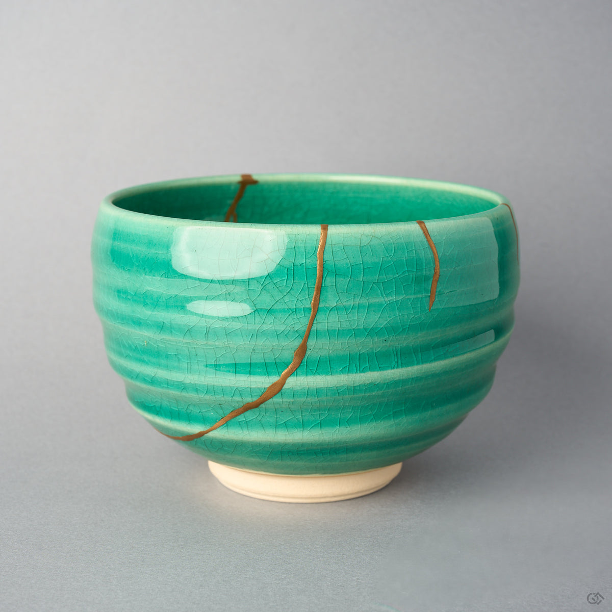 Kintsugi matcha bowl side view: two urushi and 24K gold lines descend the spiral-ridged emerald crackle glaze from the rim.