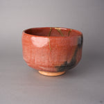 Kintsugi matcha bowl in Raku-style Kyoto ware with a smoke-grey scorch on the lower wall, rejoined with natural urushi, a thin 24K gold line at the rim.