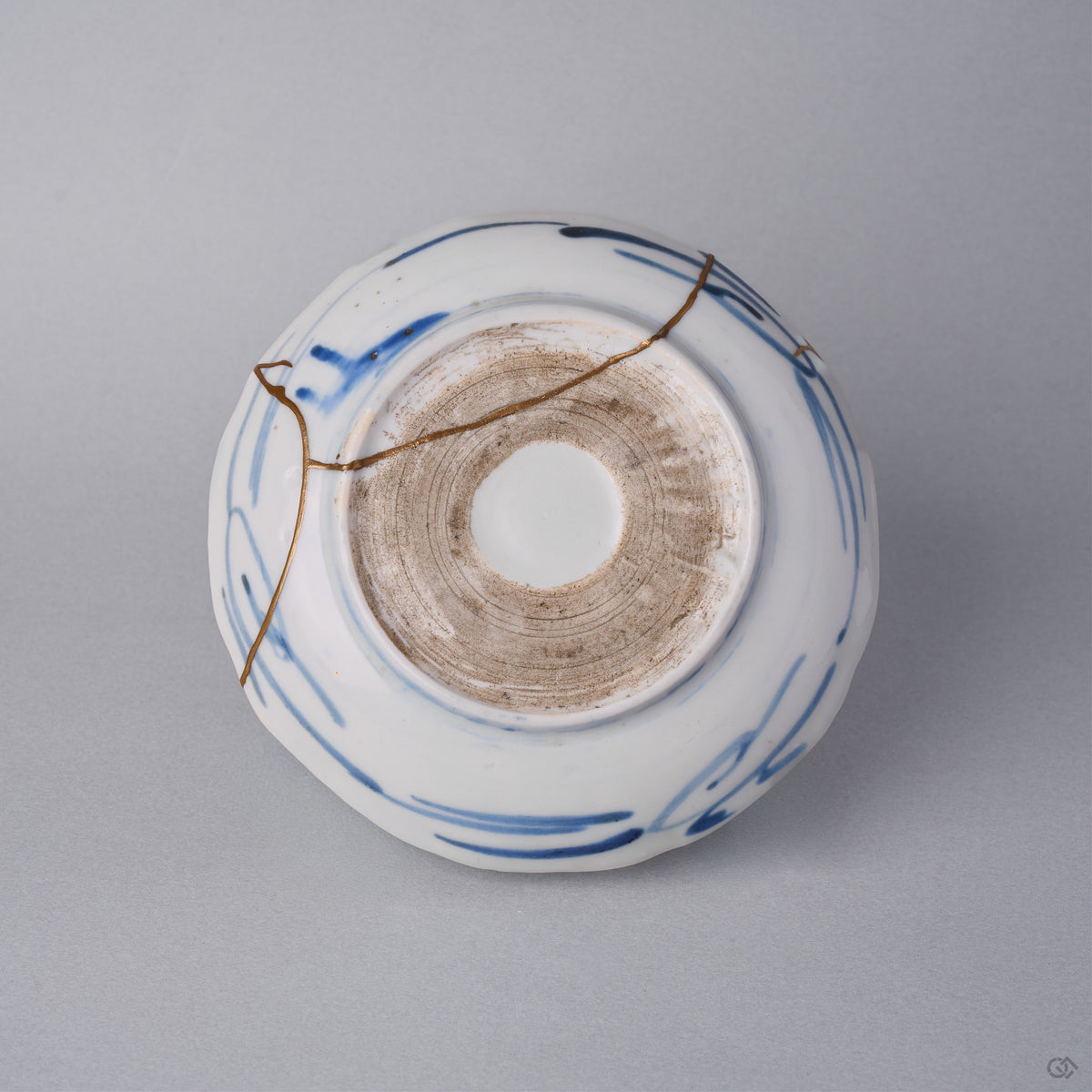 Kintsugi plate reverse in Ko-Imari porcelain, natural urushi and 24K gold seams crossing the blue brushstrokes and the unglazed foot ring of the base.