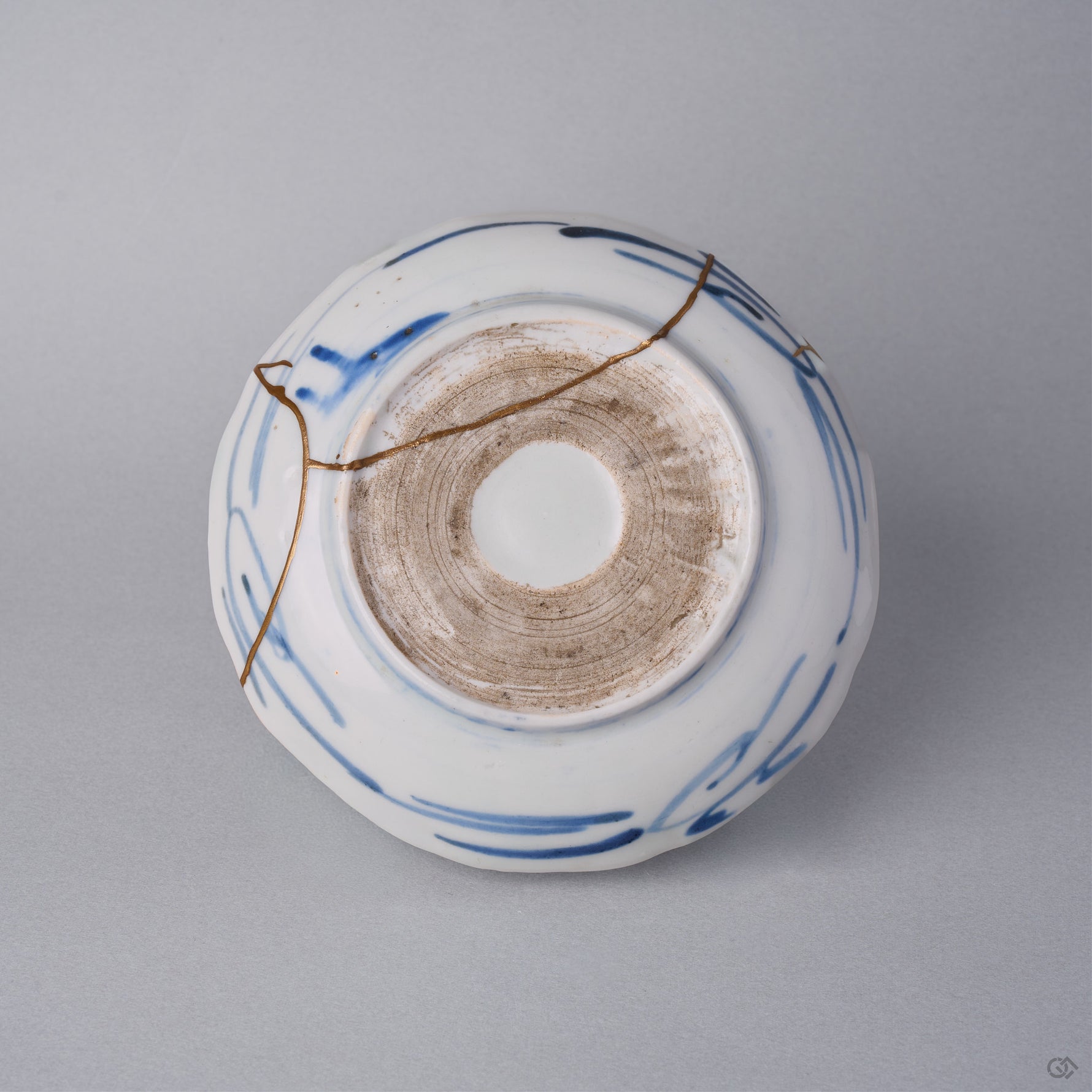 Kintsugi plate reverse in Ko-Imari porcelain, natural urushi and 24K gold seams crossing the blue brushstrokes and the unglazed foot ring of the base.