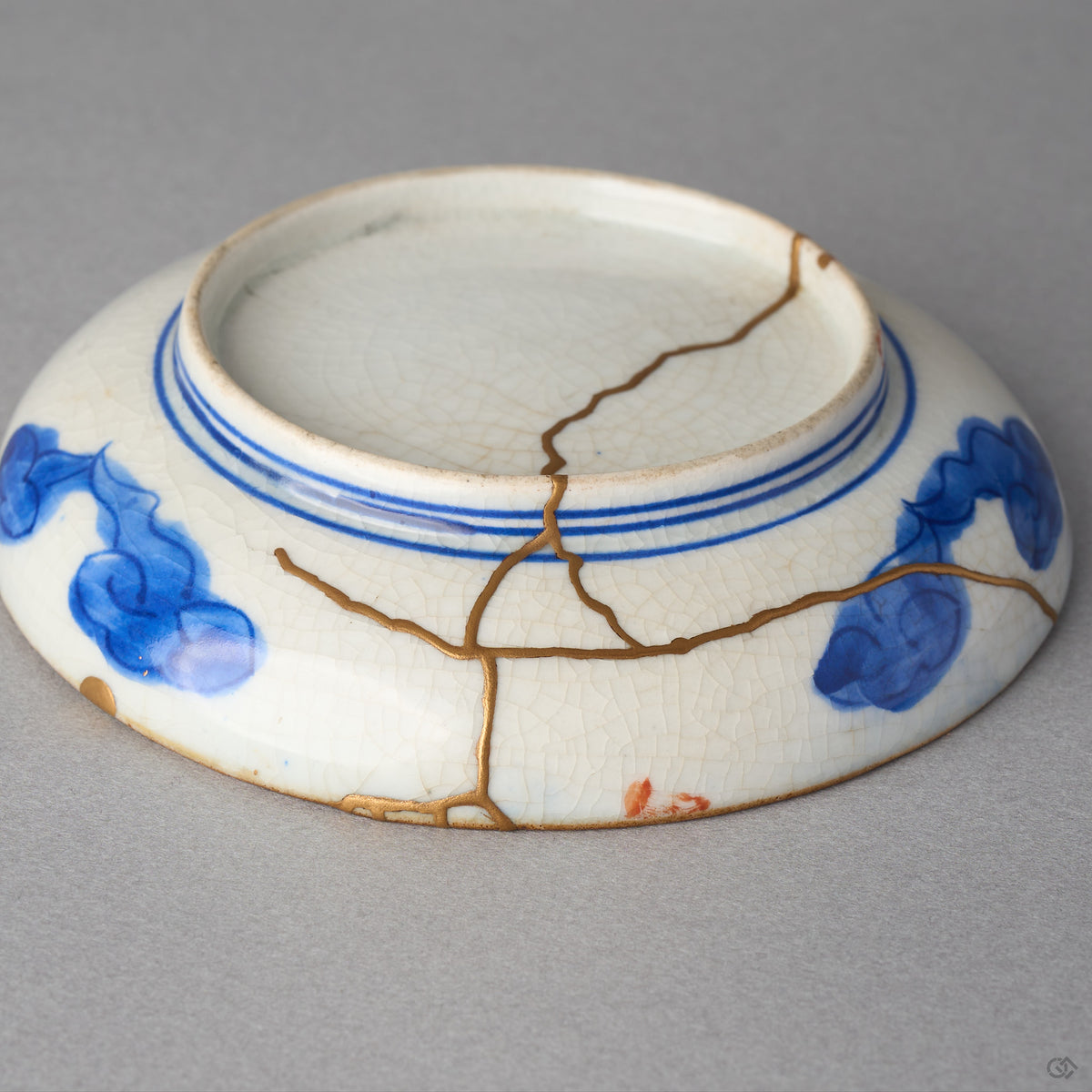 Kintsugi plate in Ko-Imari porcelain turned over, rejoined with natural urushi, branching 24K gold seams crossing the foot ring and underside, back view.