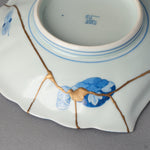 Kintsugi plate underside in Ko-Imari porcelain, rejoined with natural urushi, five 24K gold lines meeting at one point beside a blue cloud medallion, back view.