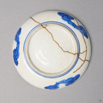 Kintsugi plate in Ko-Imari porcelain from below, rejoined with natural urushi, one 24K gold seam across the foot ring, a forked seam at the edge, bottom view.