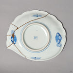 Kintsugi plate base in Ko-Imari porcelain with cloud medallions, rejoined with natural urushi, 24K gold lines meeting at one point near the edge, bottom view.