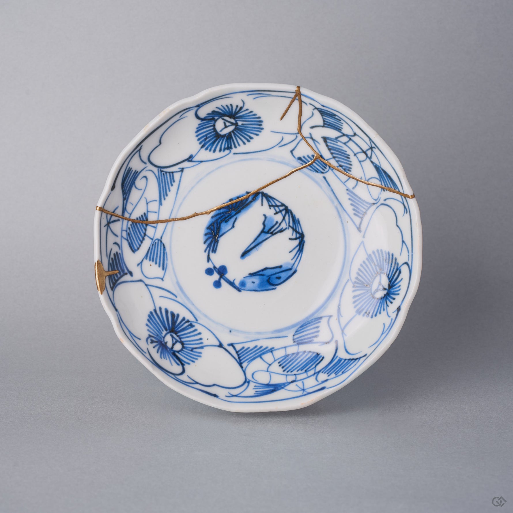 Kintsugi plate in Ko-Imari sometsuke porcelain with line-drawn camellias, a natural urushi and 24K gold seam passing through the central roundel, front view.