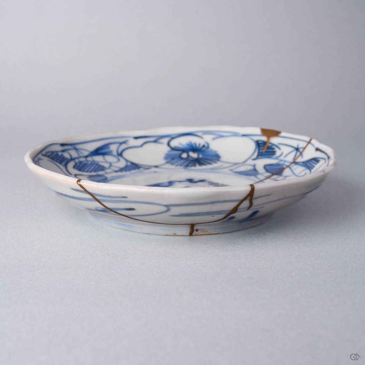 Kintsugi plate in Ko-Imari porcelain seen from the side, natural urushi and 24K gold lines running from the camellia rim down the outer wall to the foot.