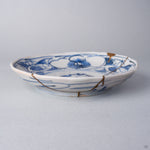 Kintsugi plate in Ko-Imari porcelain seen from the side, natural urushi and 24K gold lines running from the camellia rim down the outer wall to the foot.