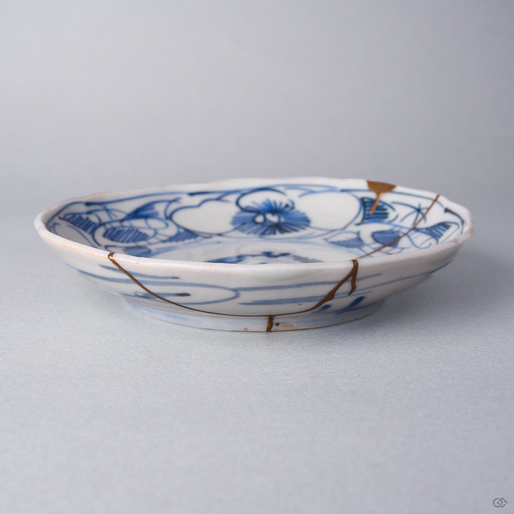 Kintsugi plate in Ko-Imari porcelain seen from the side, natural urushi and 24K gold lines running from the camellia rim down the outer wall to the foot.