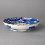 Kintsugi plate in Ko-Imari porcelain with blue clouds on the outer wall, rejoined with natural urushi, 24K gold seams meeting at the rim by a chip, side view.