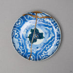 Kintsugi plate in Ko-Imari sometsuke porcelain, rejoined with natural urushi, one 24K gold seam falling from the rim across the painted night sky, front view.
