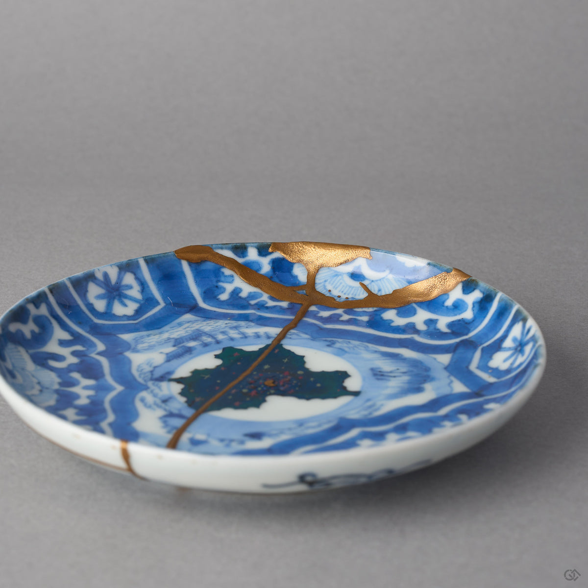Kintsugi plate in Ko-Imari porcelain at a low angle, rejoined with natural urushi, the 24K gold seam running from the rim through the urushi-e sky and stars.
