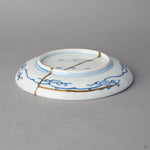 Kintsugi plate in Ko-Imari porcelain tilted to its underside, rejoined with natural urushi, a 24K gold seam along the blue karakusa border and across the foot.