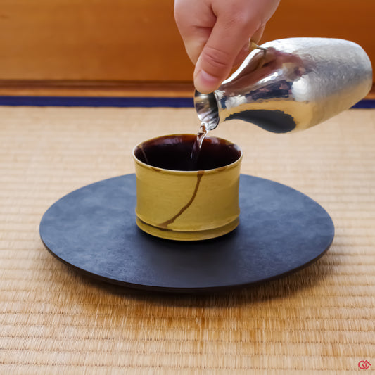 A photo of an authentic Kintsugi pottery piece being used in a real-world setting, such as a cup of sake being poured into a Kintsugi cup.