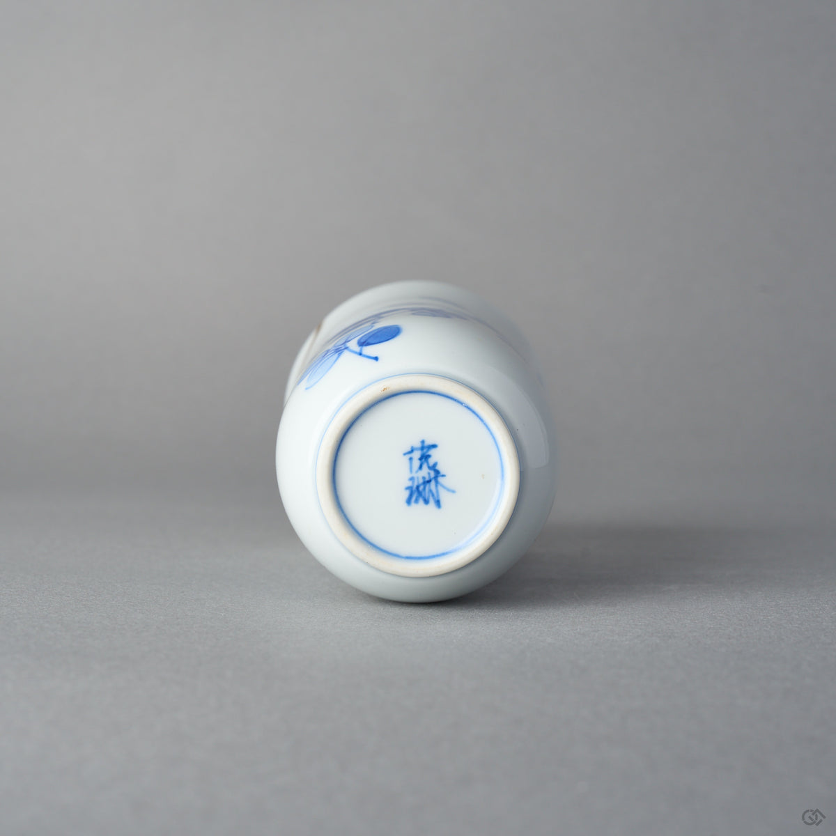 Kintsugi sake cup in Arita porcelain seen from below, a blue kiln mark on the untouched base, the natural urushi and 24K gold seam only on the upper wall.