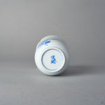 Kintsugi sake cup in Arita porcelain seen from below, a blue kiln mark on the untouched base, the natural urushi and 24K gold seam only on the upper wall.