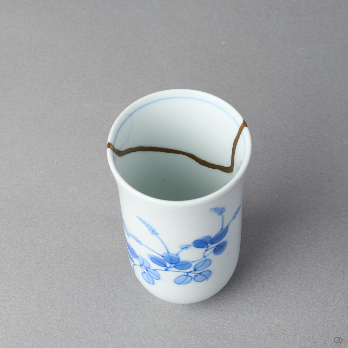 Kintsugi sake cup interior in Arita porcelain, rejoined with natural urushi, the 24K gold seam waving along the inner wall below the rim line, close-up.