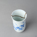 Kintsugi sake cup interior in Arita porcelain, rejoined with natural urushi, the 24K gold seam waving along the inner wall below the rim line, close-up.