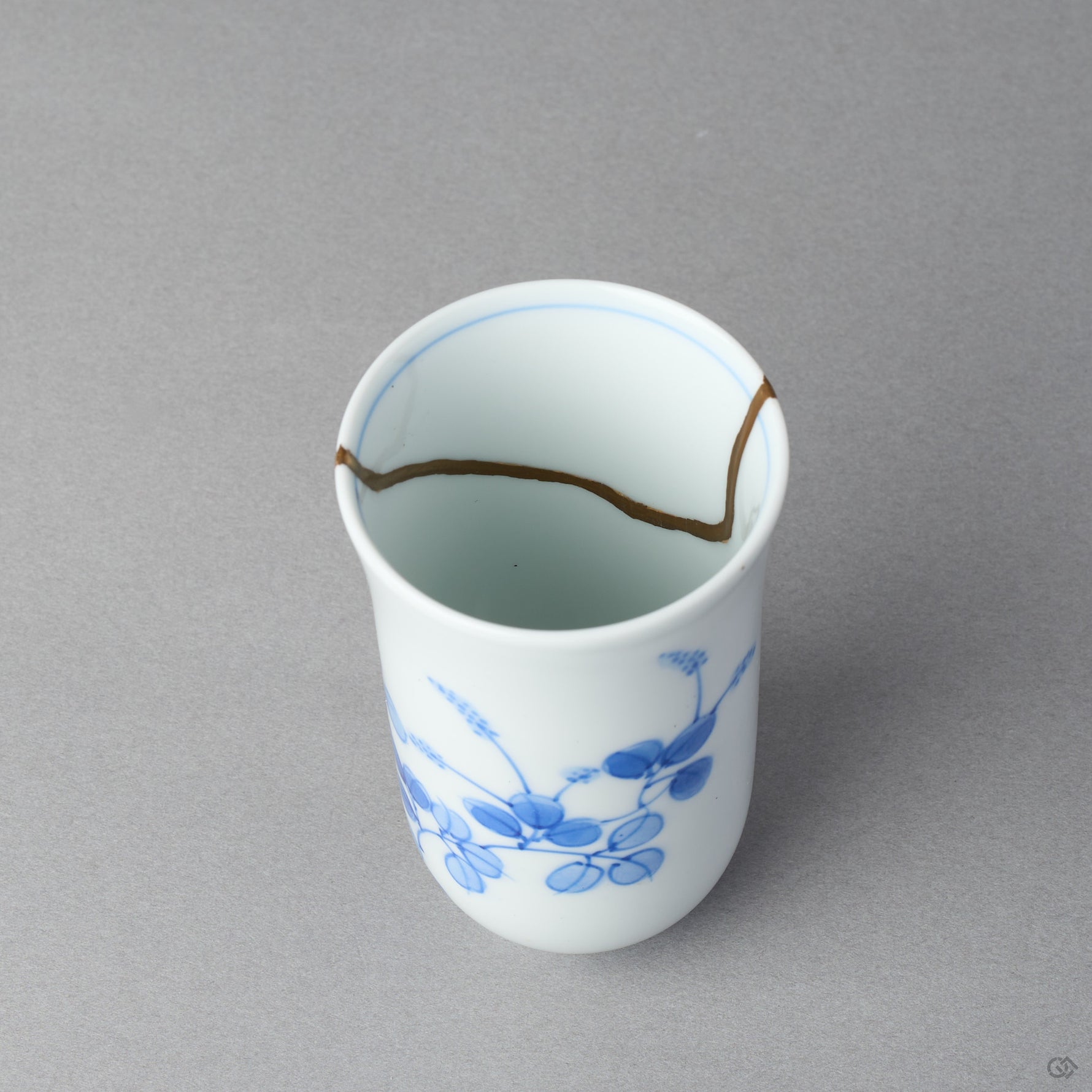 Kintsugi sake cup interior in Arita porcelain, rejoined with natural urushi, the 24K gold seam waving along the inner wall below the rim line, close-up.
