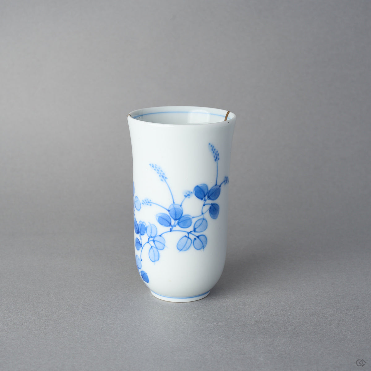 Kintsugi sake cup in Arita porcelain showing the vine of round blue leaves, rejoined with natural urushi, the 24K gold seam reaching the rim, side view.