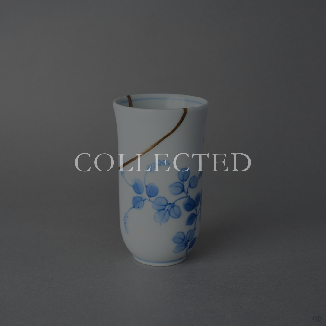 Kintsugi sake cup in thin Arita porcelain, rejoined with natural urushi and finished in 24K gold, one gold arc above the blue vine, front view. Collected.