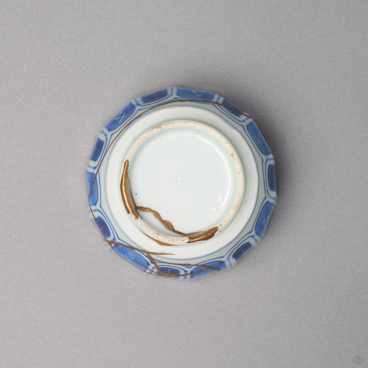 Kintsugi sake cup in Ko-Imari porcelain from below, rejoined with natural urushi, one 24K gold seam crossing the foot ring and the base, bottom view.