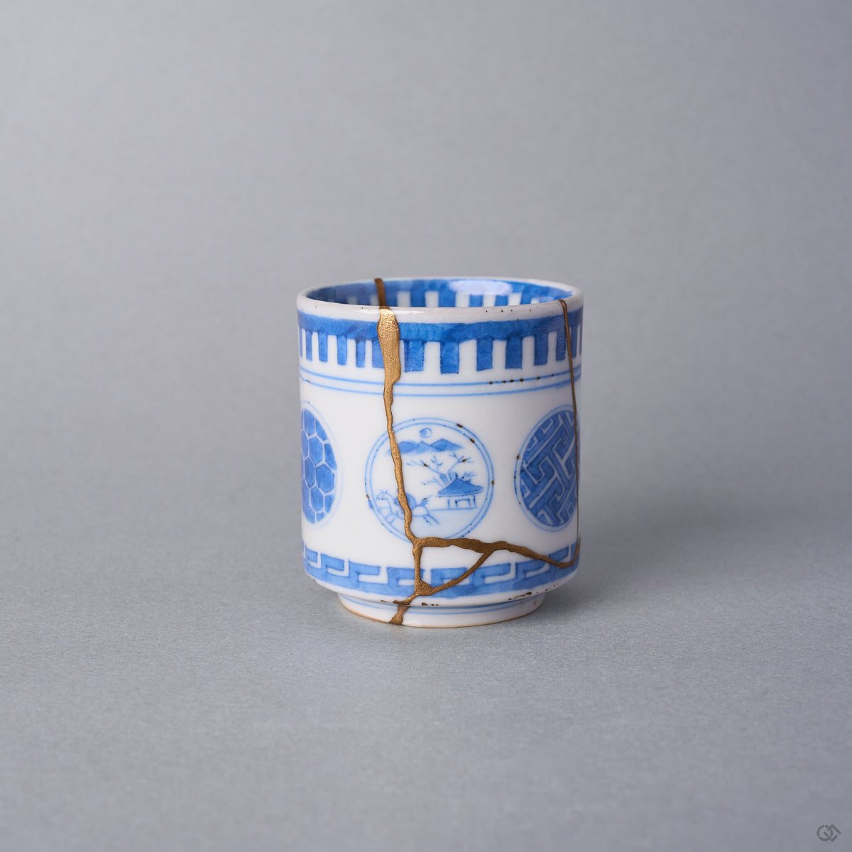 Kintsugi sake cup in Ko-Imari sometsuke porcelain, a natural urushi and 24K gold seam descending between the tortoiseshell and landscape windows, front view.