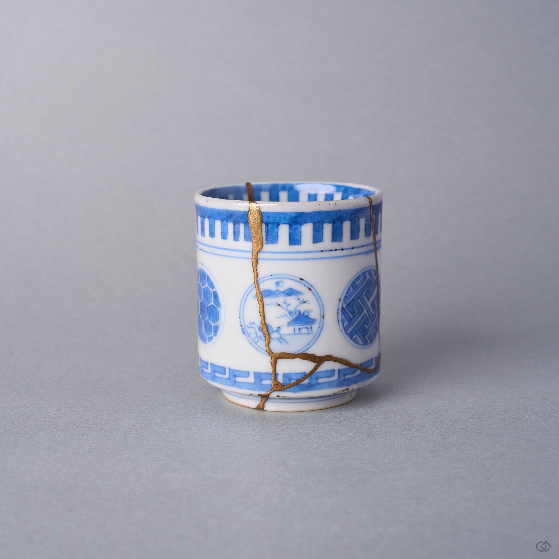 Kintsugi sake cup in Ko-Imari sometsuke porcelain, a natural urushi and 24K gold seam descending between the tortoiseshell and landscape windows, front view.