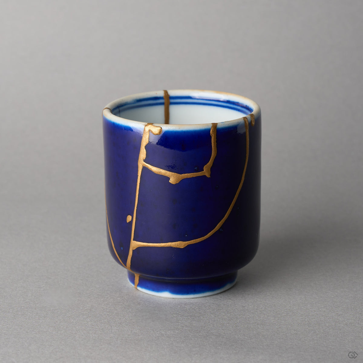 Kintsugi sake cup in lapis-blue Ko-Imari porcelain, rejoined with natural urushi, 24K gold seams framing the front, front view.
