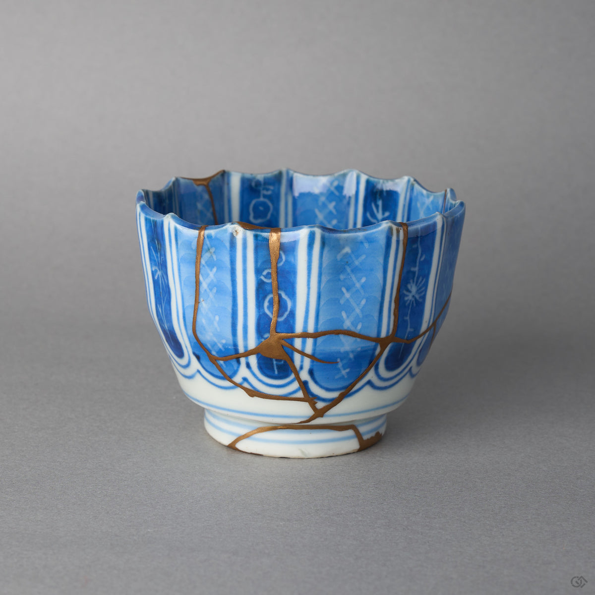 Kintsugi sake cup in fluted Ko-Imari porcelain, rejoined with natural urushi, 24K gold seams meeting at one point low on the blue columns, front view.