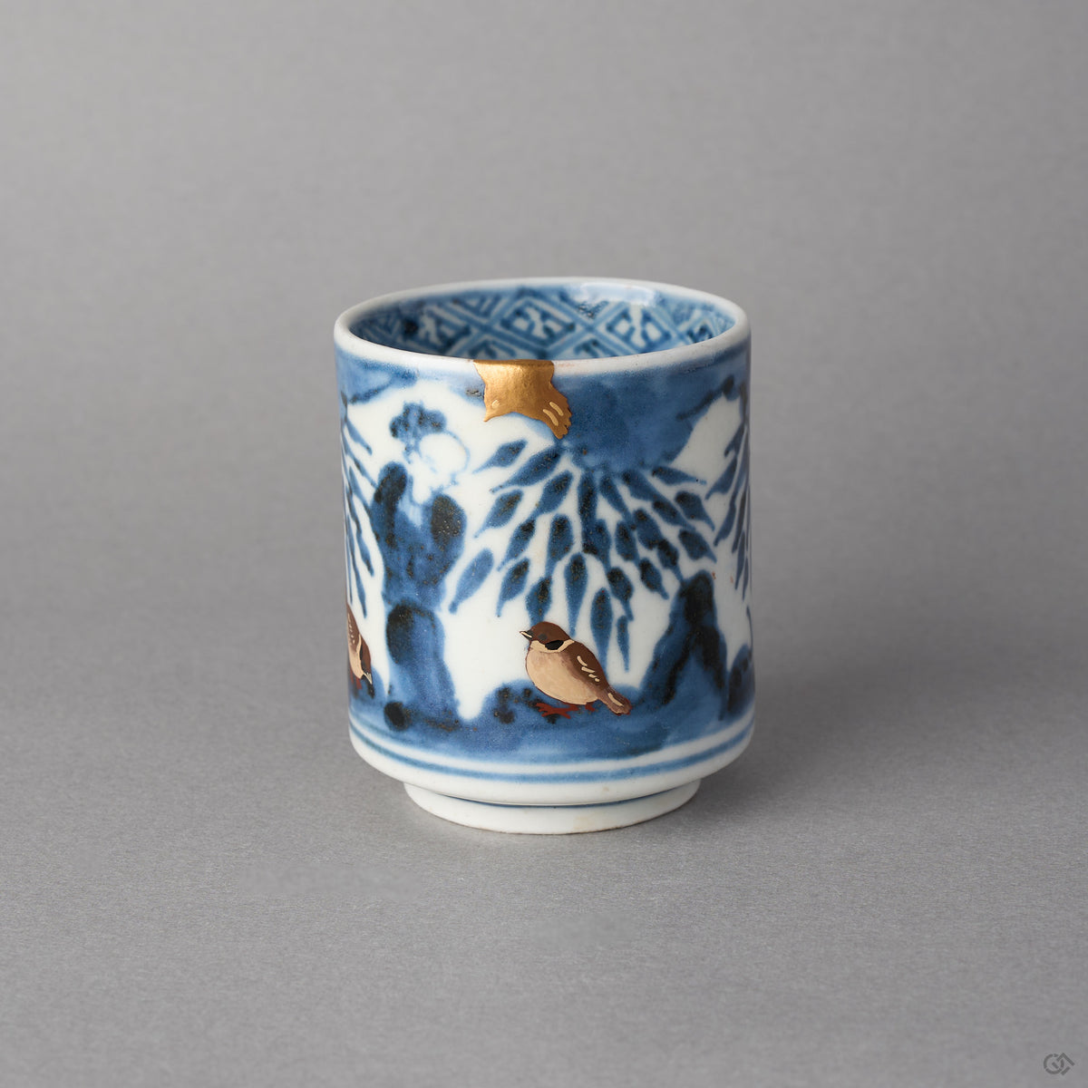 Kintsugi sake cup in Ko-Imari porcelain with a cobalt figure beneath bamboo, the rim rebuilt in natural urushi under a 24K gold sparrow, front view.