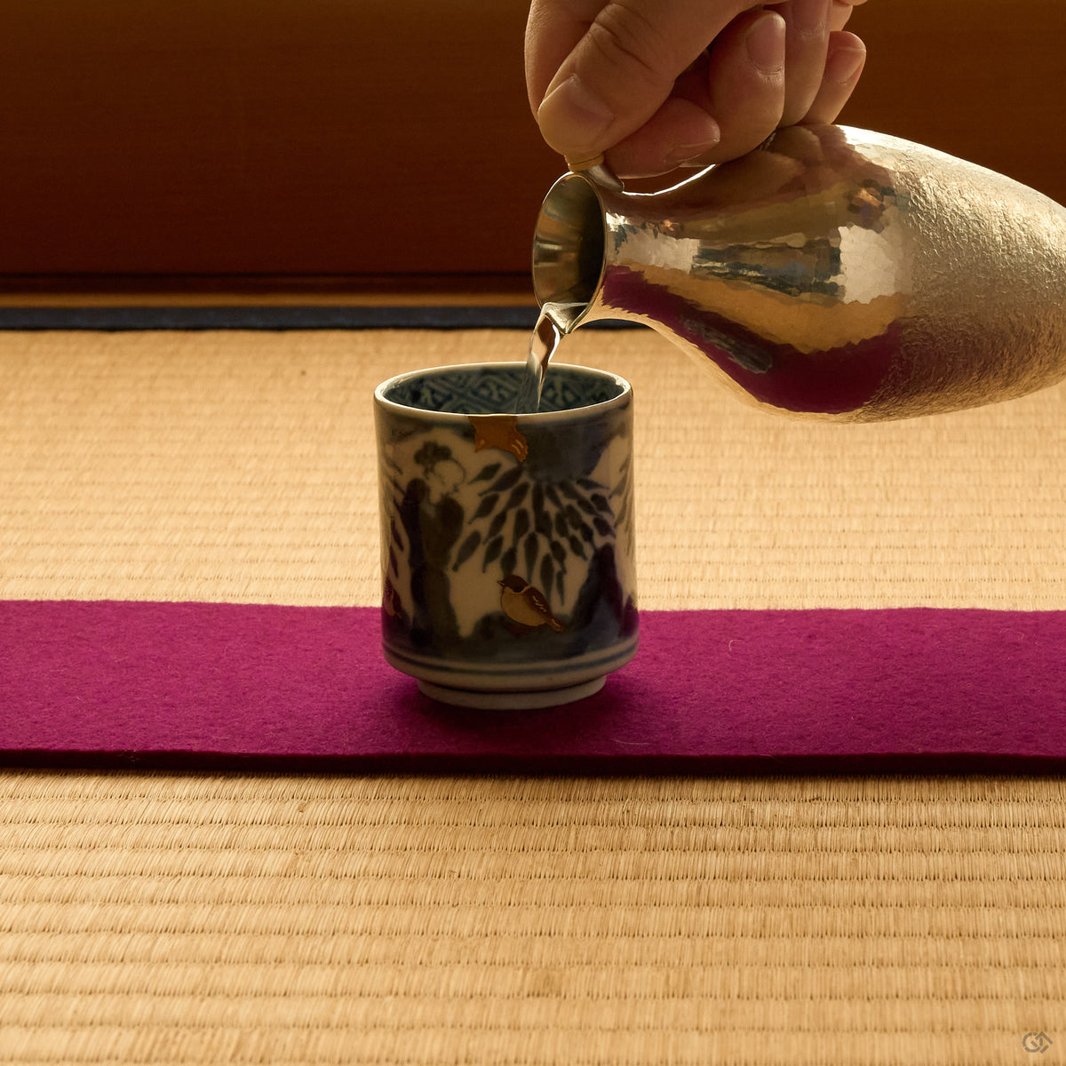 Kintsugi sake cup in Ko-Imari porcelain on tatami, sake poured from a hammered tin flask, the rim rebuilt in natural urushi under a 24K gold sparrow.